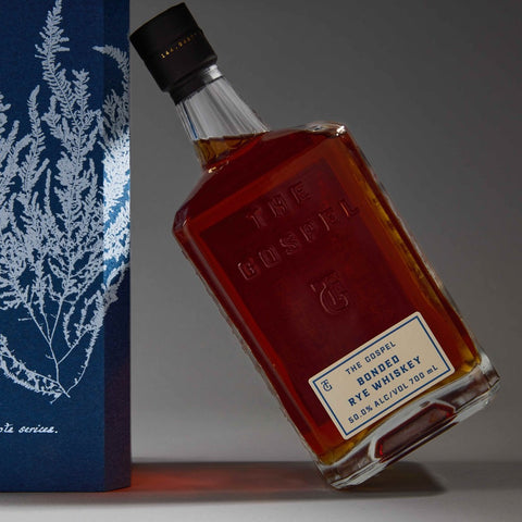 The Gospel Bonded Rye Whiskey 50% bottle leaning against the cyanotype gift box